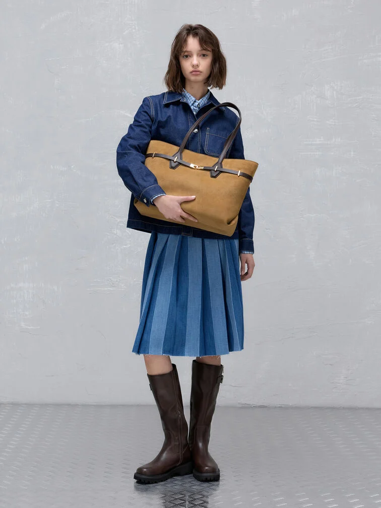 Knee-high boots paired with a pleated denim skirt creates a polished preppy aesthetic — complete the look with a sophisticated suede tote bag 