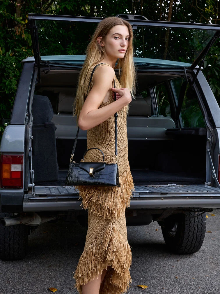 Black elongated top handle bag paired with an elegant warm-toned dress.